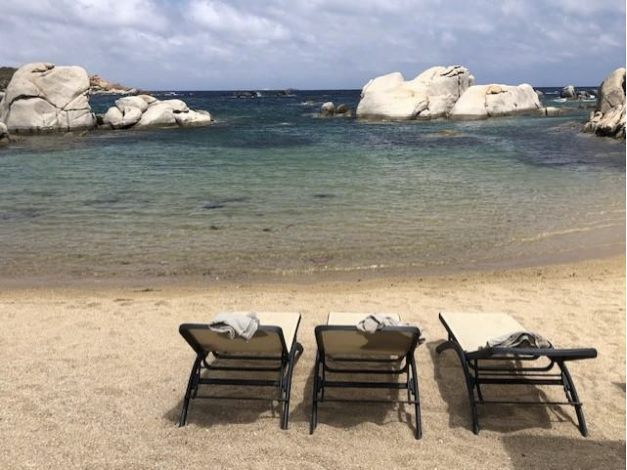 Three beach chairs sit on the white sand beach in front of the sea in Sardinia 